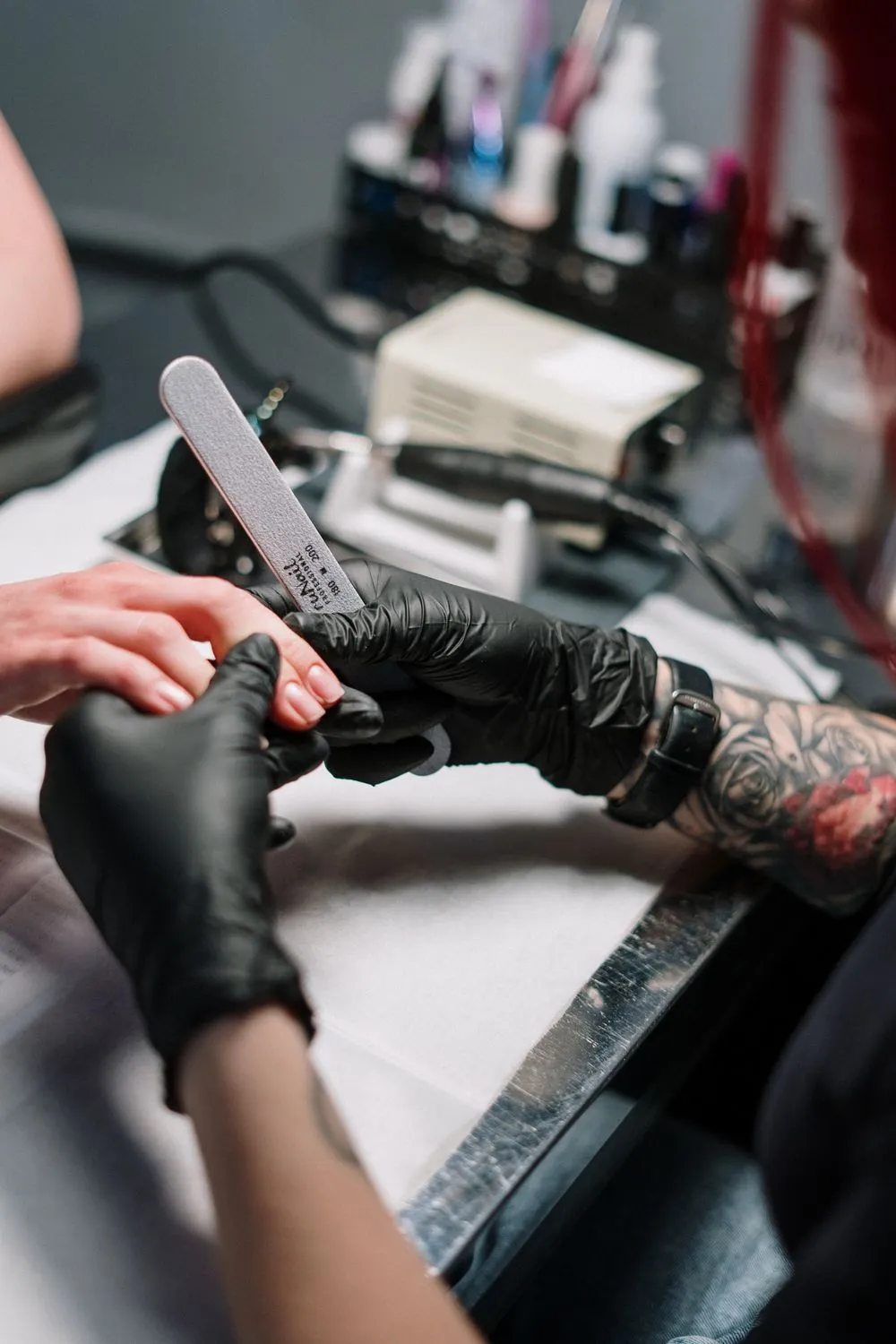Uma profissional de unhas a limar cuidadosamente as unhas de uma cliente